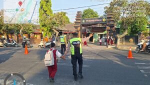 Anggota Polsek Wlingi membantu menyeberangkan pelajar saat melaksanakan strong point pagi di depan SDN Babadan 01, Wlingi, Blitar, Selasa (6/10/2026).