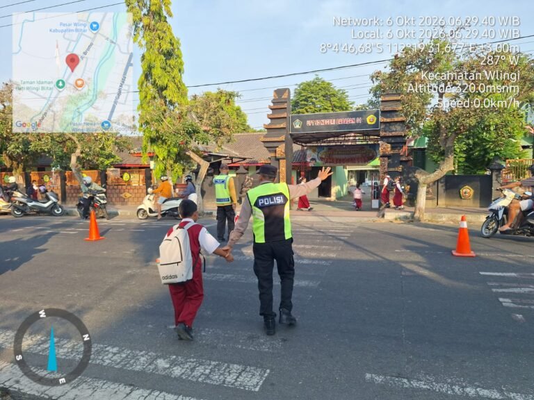 Anggota Polsek Wlingi membantu menyeberangkan pelajar saat melaksanakan strong point pagi di depan SDN Babadan 01, Wlingi, Blitar, Selasa (6/10/2026).